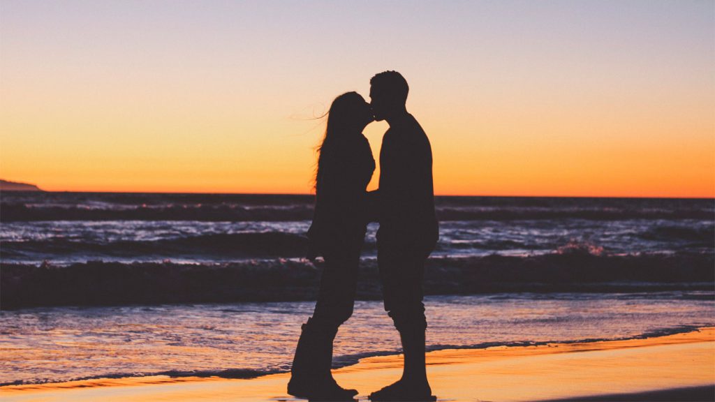Silhouetted couple kissing as the waves roll in on the beach at sunset