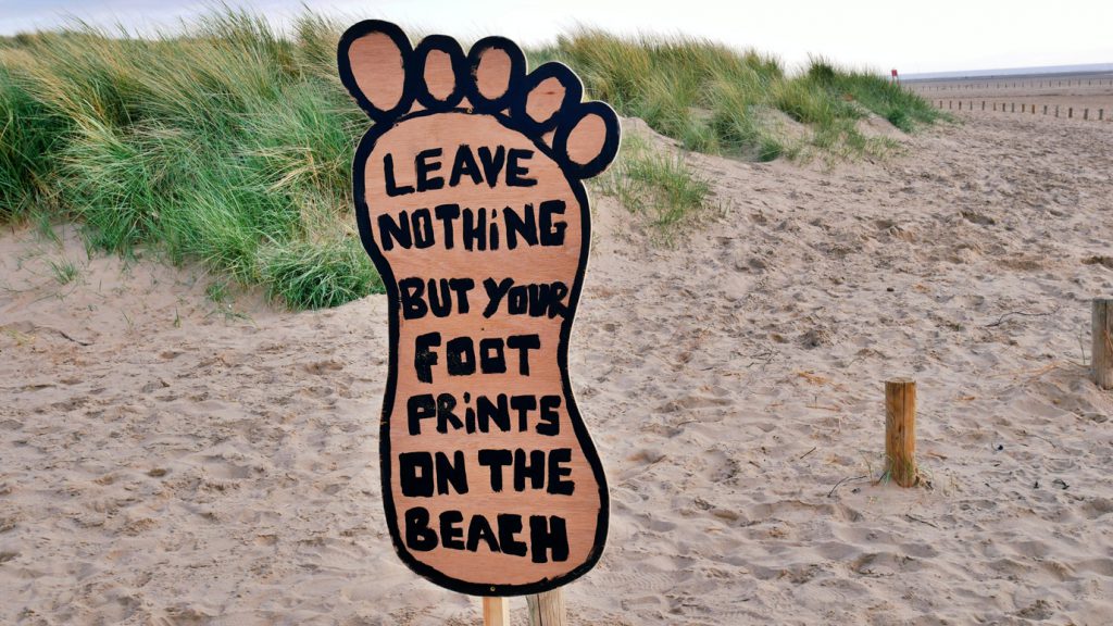 Foot-shaped sign on sandy beach that says to only leave footprints