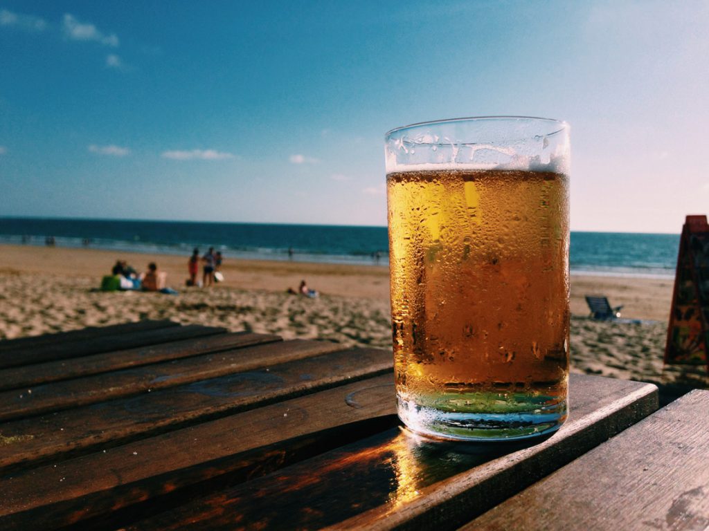 A cold beer in a mug on a wood table at the sunny beach
