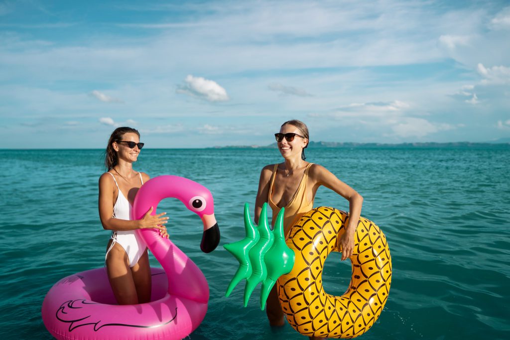 Friends at the beach in the water holding floaties